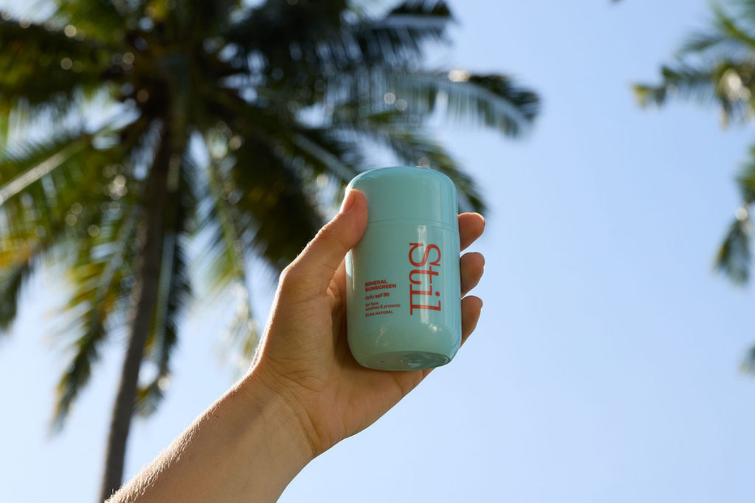 Hand holding a bottle of sunscreen with a background of blue sky and palm trees